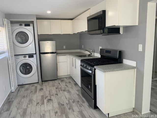 kitchen with sink, appliances with stainless steel finishes, stacked washer and clothes dryer, and white cabinetry