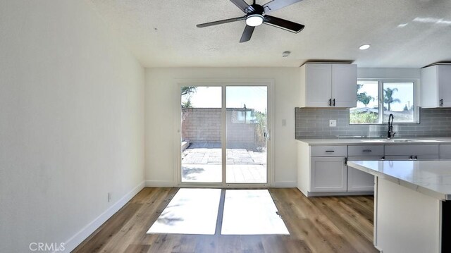 kitchen featuring sink, ceiling fan, light hardwood / wood-style floors, decorative backsplash, and white cabinets
