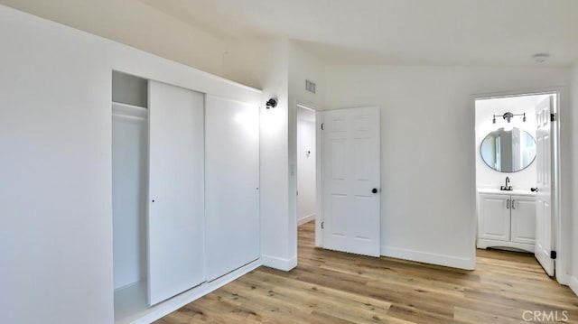 unfurnished bedroom featuring vaulted ceiling, connected bathroom, sink, light wood-type flooring, and a closet