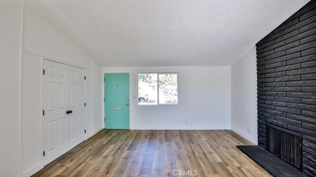 unfurnished living room featuring lofted ceiling, a brick fireplace, and light hardwood / wood-style floors