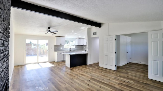 kitchen featuring lofted ceiling with beams, a textured ceiling, light hardwood / wood-style floors, decorative backsplash, and white cabinets