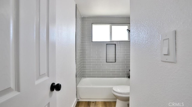 bathroom with tiled shower / bath combo, wood-type flooring, and toilet