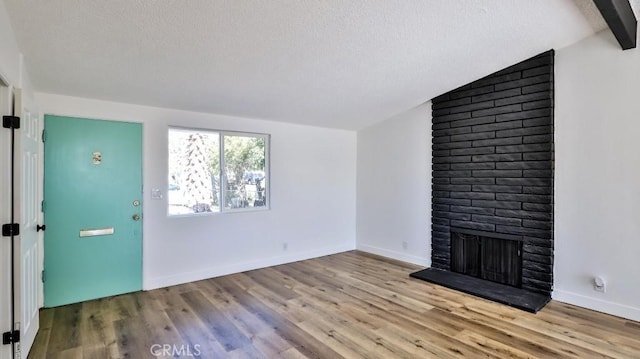 unfurnished living room with a brick fireplace, a textured ceiling, light hardwood / wood-style flooring, and vaulted ceiling with beams