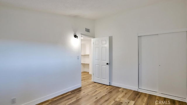unfurnished bedroom with vaulted ceiling, light hardwood / wood-style floors, and a closet