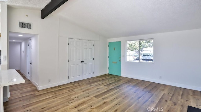 foyer with lofted ceiling with beams, hardwood / wood-style flooring, and a textured ceiling