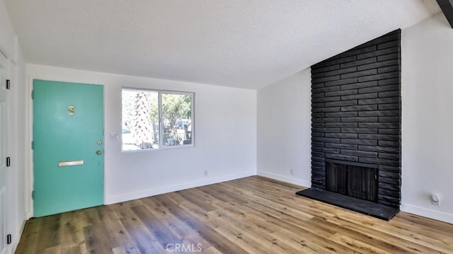 unfurnished living room with vaulted ceiling, a textured ceiling, a fireplace, and light hardwood / wood-style flooring