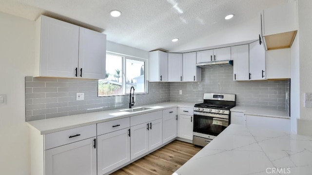 kitchen with sink, stainless steel gas range, white cabinetry, light stone counters, and vaulted ceiling