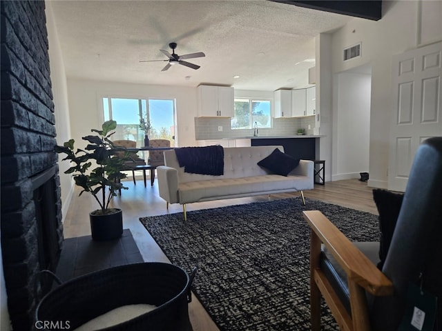 living room featuring ceiling fan, light hardwood / wood-style flooring, beamed ceiling, and a textured ceiling