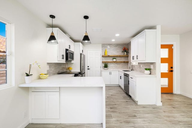 kitchen with sink, white cabinets, hanging light fixtures, kitchen peninsula, and stainless steel appliances