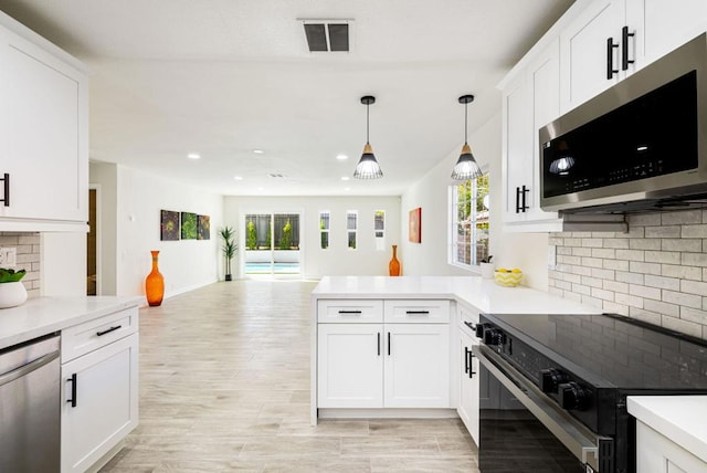 kitchen featuring hanging light fixtures, appliances with stainless steel finishes, white cabinets, and kitchen peninsula