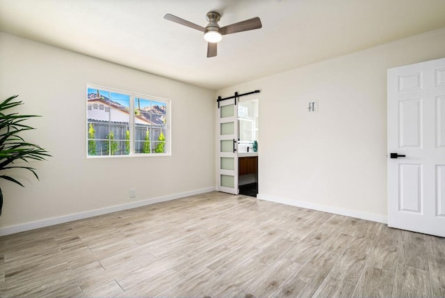 spare room featuring a barn door, ceiling fan, and light wood-type flooring