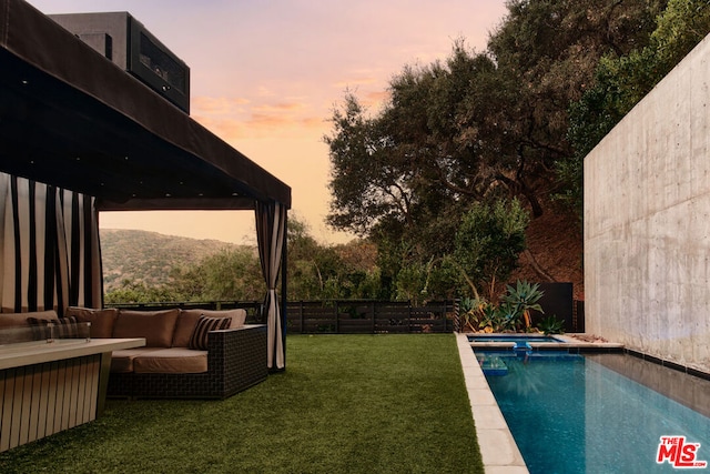 pool at dusk with a lawn and an outdoor living space