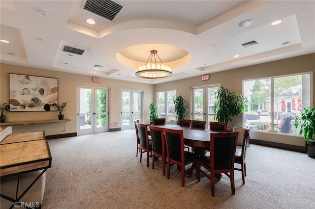 carpeted dining room with french doors, a tray ceiling, and a chandelier