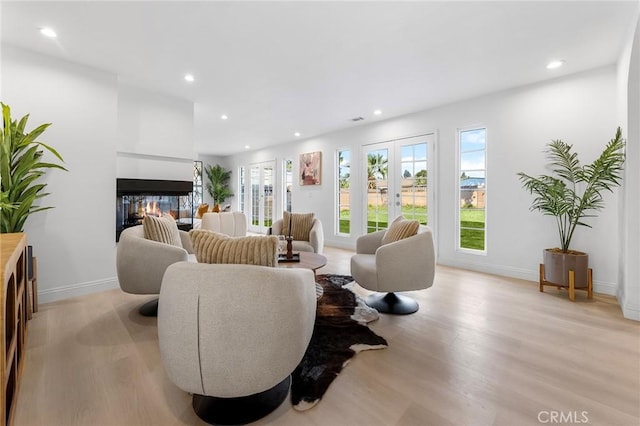 living room with a multi sided fireplace, french doors, and light wood-type flooring