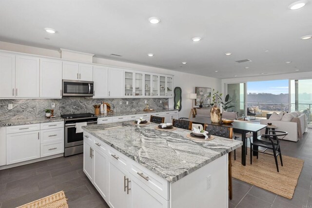 kitchen with appliances with stainless steel finishes, a kitchen island, light stone counters, and tasteful backsplash