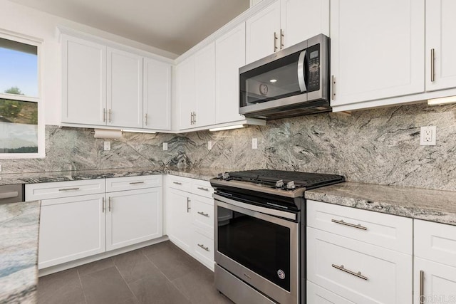 kitchen featuring stainless steel appliances, backsplash, white cabinets, light stone countertops, and dark tile patterned flooring