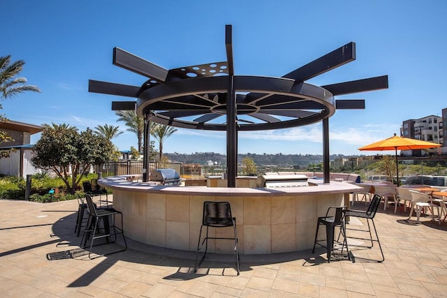 view of patio with an outdoor kitchen, outdoor wet bar, a grill, fence, and a pergola