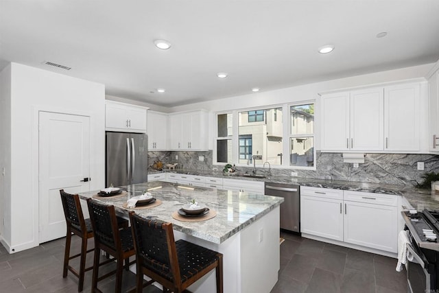 kitchen with light stone counters, appliances with stainless steel finishes, white cabinets, a sink, and a kitchen bar