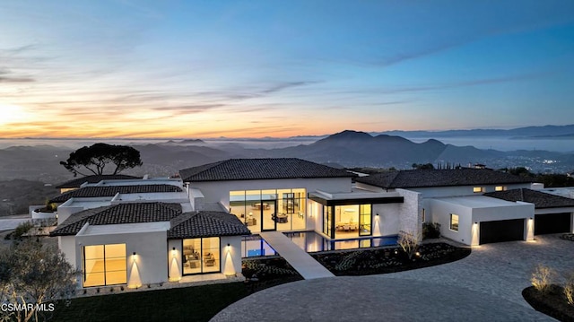 back house at dusk with a mountain view and a garage