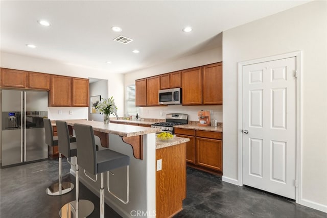 kitchen featuring stainless steel appliances, a kitchen island, a breakfast bar area, and light stone countertops