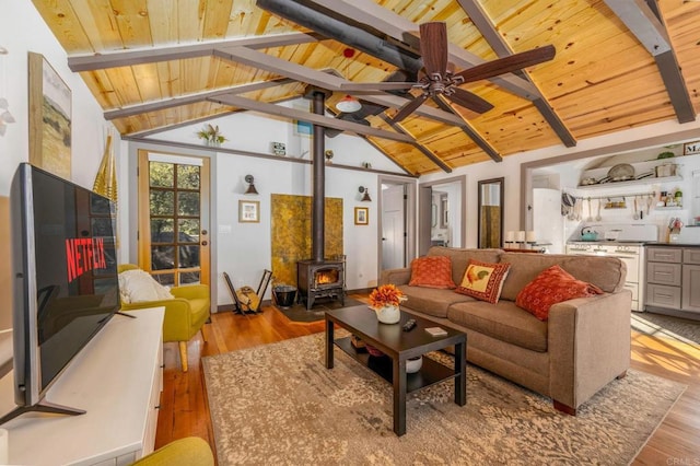 living room featuring vaulted ceiling with beams, light hardwood / wood-style flooring, ceiling fan, and a wood stove