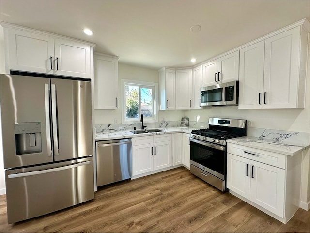 kitchen with light stone countertops, white cabinetry, stainless steel appliances, light hardwood / wood-style floors, and sink