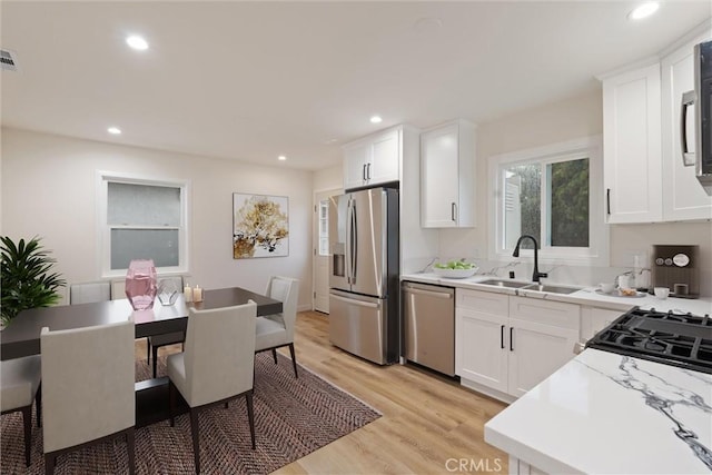 kitchen with sink, light wood-type flooring, white cabinets, and appliances with stainless steel finishes