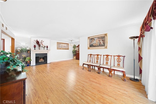 living area featuring a fireplace with flush hearth, ornamental molding, light wood-style flooring, and baseboards