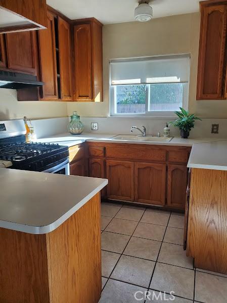 kitchen featuring sink, light tile patterned floors, stainless steel gas range, and kitchen peninsula