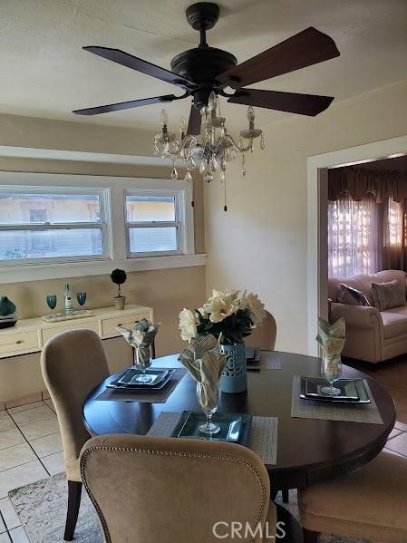 tiled dining space with ceiling fan with notable chandelier and a healthy amount of sunlight