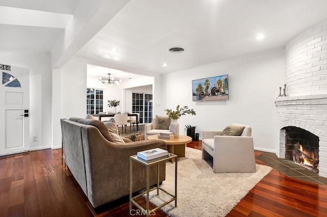 living room with dark hardwood / wood-style floors, a brick fireplace, and a notable chandelier