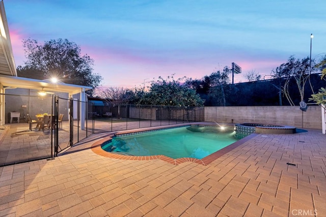 pool at dusk with an in ground hot tub and a patio