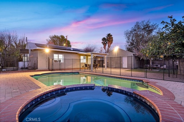 pool at dusk with a patio area and an in ground hot tub