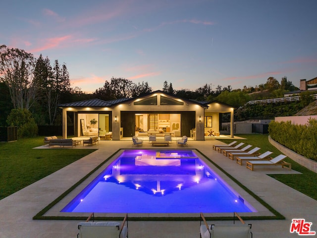 pool at dusk with outdoor lounge area, a patio area, and a lawn