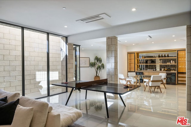 game room with a wall of windows, light tile patterned floors, and decorative columns