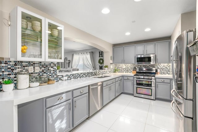 kitchen featuring gray cabinetry, sink, light tile patterned floors, appliances with stainless steel finishes, and tasteful backsplash