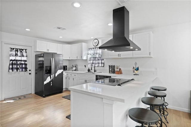 kitchen featuring white cabinets, stainless steel fridge, a kitchen bar, and island exhaust hood