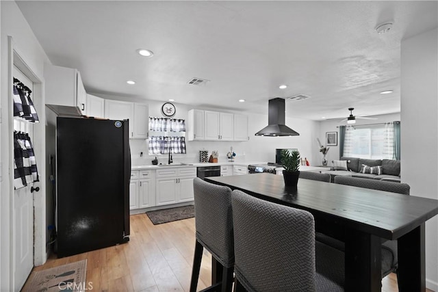 kitchen with light wood-type flooring, island range hood, ceiling fan, black appliances, and white cabinets