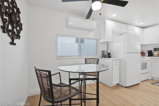 kitchen with white appliances, ceiling fan, a wall mounted AC, light hardwood / wood-style floors, and white cabinetry