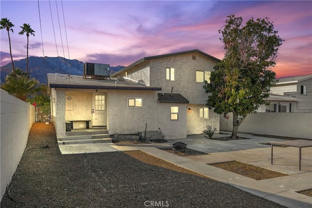 back house at dusk with a mountain view, a patio, and central AC