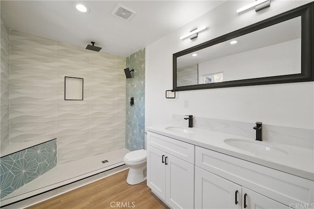 bathroom featuring vanity, a baseboard heating unit, tiled shower, hardwood / wood-style flooring, and toilet