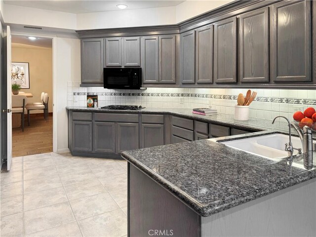 kitchen featuring dark brown cabinets, light tile patterned floors, sink, and dark stone counters