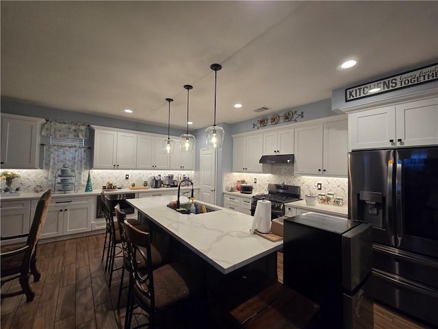 kitchen featuring black fridge with ice dispenser, a kitchen island with sink, sink, pendant lighting, and stainless steel range with gas stovetop