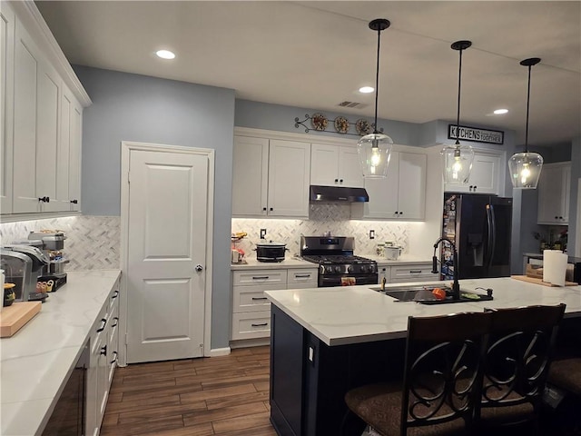 kitchen with black fridge with ice dispenser, a kitchen island with sink, stainless steel gas stove, hanging light fixtures, and a breakfast bar area