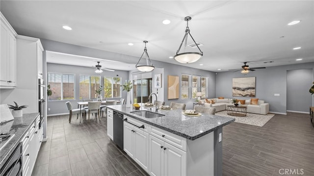 kitchen with a kitchen island with sink, sink, dark stone counters, and white cabinets