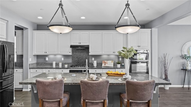 kitchen with hanging light fixtures, an island with sink, white cabinets, and black fridge