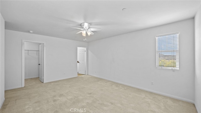 unfurnished bedroom featuring light carpet, a spacious closet, a closet, and ceiling fan