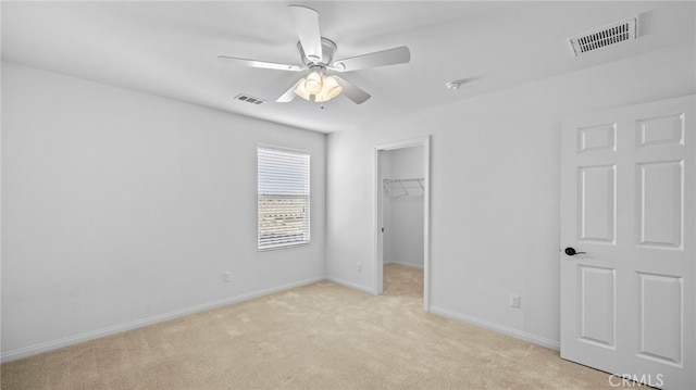 unfurnished bedroom with a spacious closet, light colored carpet, a closet, and ceiling fan