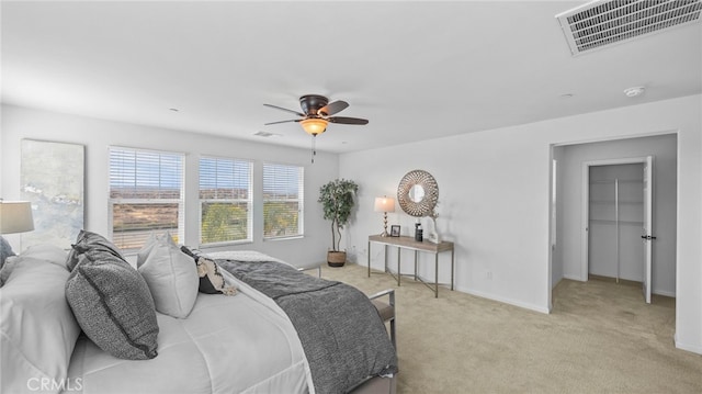 bedroom featuring a walk in closet, light colored carpet, and ceiling fan