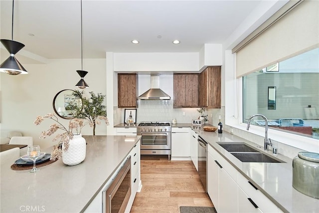 kitchen featuring stainless steel appliances, sink, wall chimney range hood, pendant lighting, and white cabinetry